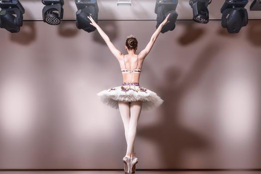 Young graceful ballerina in image of white swan in art performance . Back view. Dance on the tips of toes.