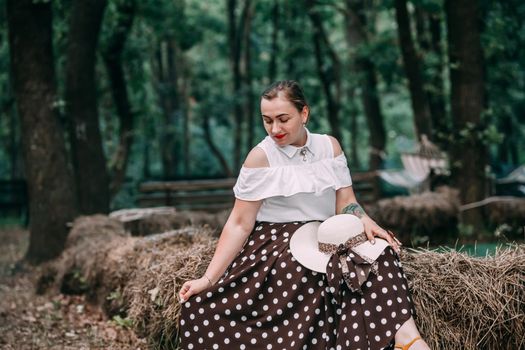 photo of a young smiling blonde, in a white blouse and skirt, on the hay in a summer forest.