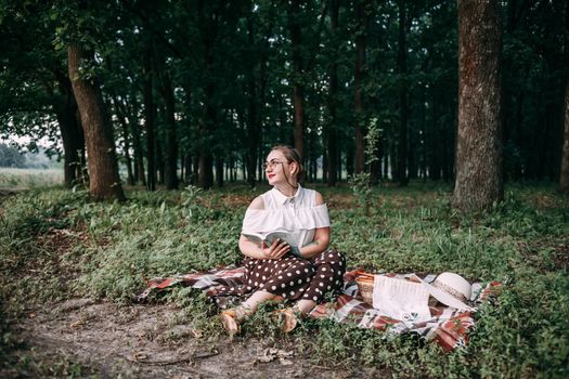 a girl with glasses reads a book in a summer forest