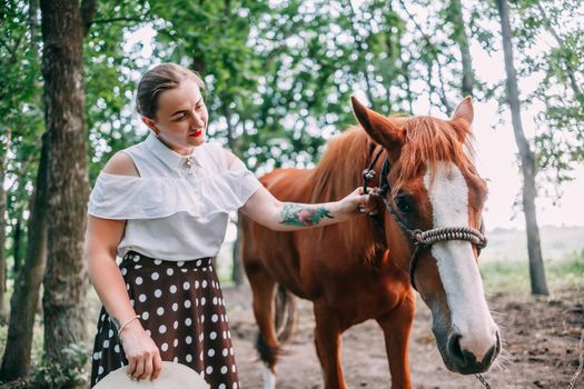 photo of a young smiling blonde, in a white blouse and skirt, with a horse, in a summer forest.