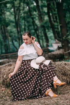 photo of a young smiling blonde, in a white blouse and skirt, on the hay in a summer forest.