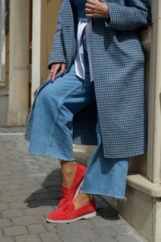 Woman in a red stylish suede loafer shoes, blue jeanse, white shirt and trendy checkered coat. Pair of trendy female loafers shoes, outdoors