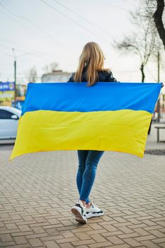 Portrait of a joyful Ukrainian woman holding a Ukrainian flag and a sign. The girl is waiting for her husband from the war. War between Russia and Ukraine