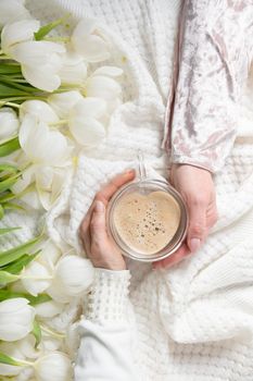 hands of two women holding a heart-shaped cup with cappuccino on two sides, female friendship, flat lay with white tulips, mother's day, valentine's day,