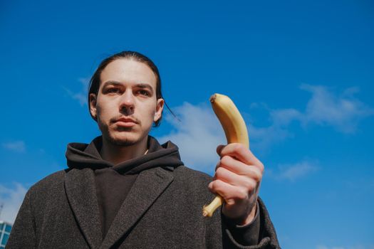 killer man with a banana instead of a gun. angry and confident look. Portrait of a nerd with mustache holding a banana weapon in his hand.