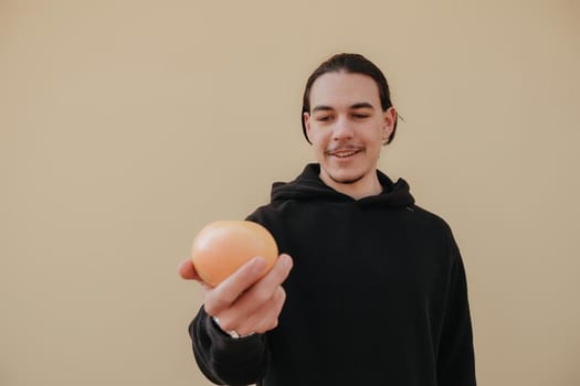 Young handsome tall slim white man with black hair balancing oranges in red shirt on yellow background. gay hipster