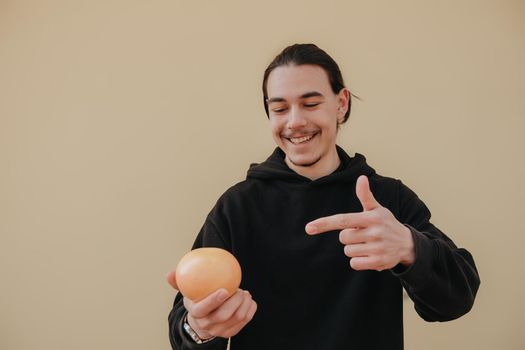 Young handsome tall slim white man with black hair balancing oranges in red shirt on yellow background. gay hipster