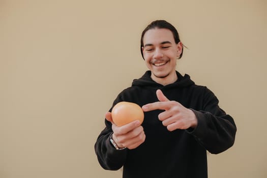 Young handsome tall slim white man with black hair balancing oranges in red shirt on yellow background. gay hipster