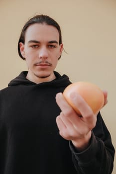 Young handsome tall slim white man with black hair balancing oranges in red shirt on yellow background. gay hipster