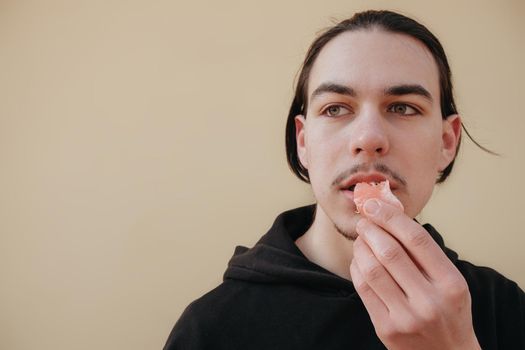 young Caucasian guy bites sour unripe citrus. A man makes a face because of the sour taste of fruit, posing on a green background. Vitamin C. Weak sensitive tooth enamel.