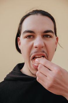 young Caucasian guy bites sour unripe citrus. A man makes a face because of the sour taste of fruit, posing on a green background. Vitamin C. Weak sensitive tooth enamel.