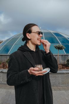 Young gay hipster eating peanuts at the street smiling happy sunglasses. Healthy lifestyle