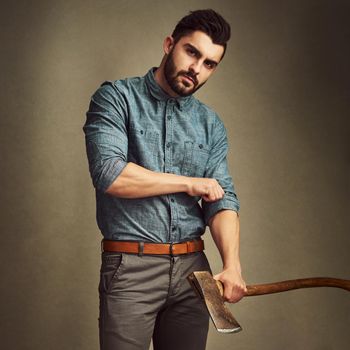 Studio shot of a young man posing with an axe against a green background.