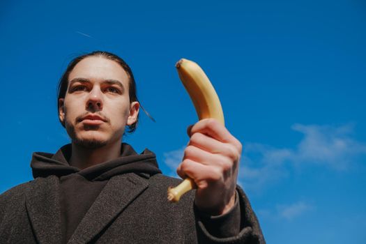 killer man with a banana instead of a gun. angry and confident look. Portrait of a nerd with mustache holding a banana weapon in his hand.