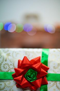 A large red bow on a Christmas gift. A decorative box with a Christmas gift in the background with cork lights.