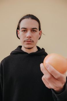 Young handsome tall slim white man with black hair balancing oranges in red shirt on yellow background. gay hipster