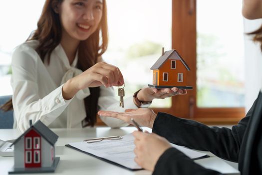 Real estate agent holding house key to his client after signing contract agreement in office,concept for real estate, moving home or renting property.
