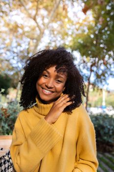 Vertical portrait of smiling young African American woman looking at camera outdoors. Lifestyle concept.