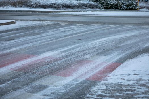 Uncleared street and pedestrian crossing of snow and frozen ice. More dangerously slippery at the pedestrian crossing.