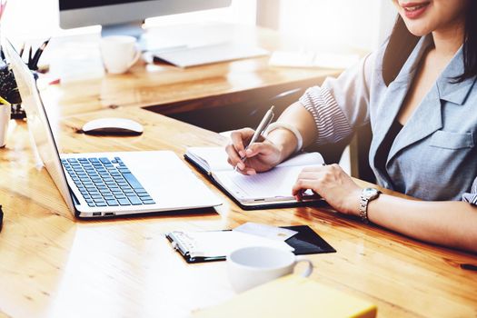 learning, note taking, planning, female employee holding a pen to write a notebook and using a computer to learn how to plan, invest and manage financial risks