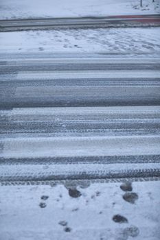 Uncleared street and pedestrian crossing of snow and frozen ice. More dangerously slippery at the pedestrian crossing.