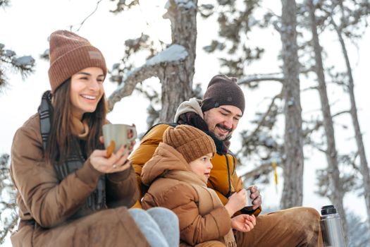 Happy family with cups of hot tea spending time together in winter forest, close up