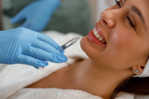 Smiling young woman getting hyaluronic acid injections in lips at beauty salon. Cosmetology