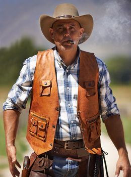 A mature cowboy outdoors with his gun drawn.