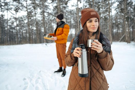 Young woman with hot drink thermos at winter forest, close up