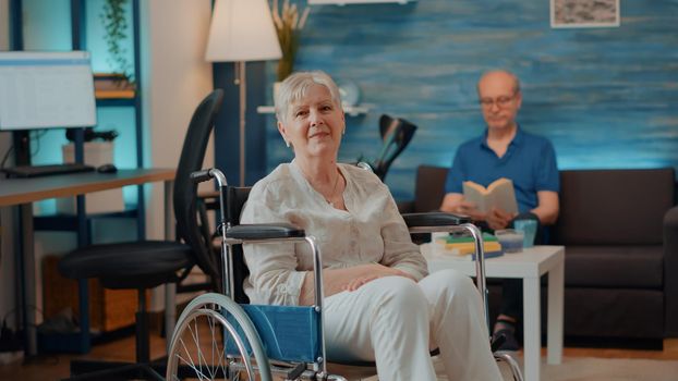 Portrait of retired woman sitting in wheelchair at home. Senior person dealing with physical disability and receiving transportation support to help with chronic problem. Pensioner smiling
