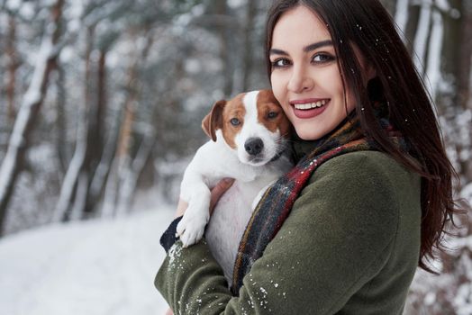 Nice portrait. Smiling brunette having fun while walking with her dog in the winter park.