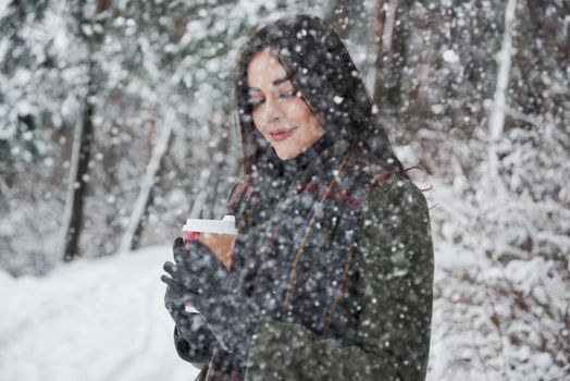 Joyful moment. Girl in warm clothes with cup of coffee have a walk in the winter forest.