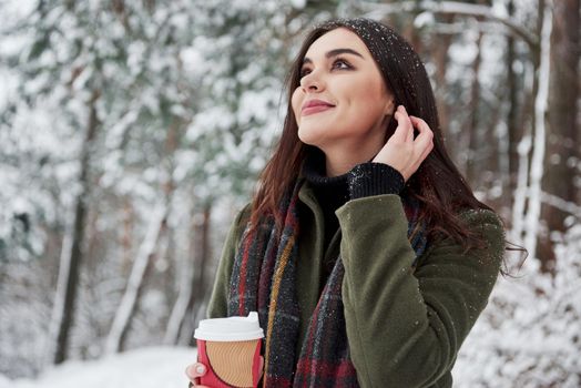 Close up portrait. Girl in warm clothes with cup of coffee have a walk in the winter forest.