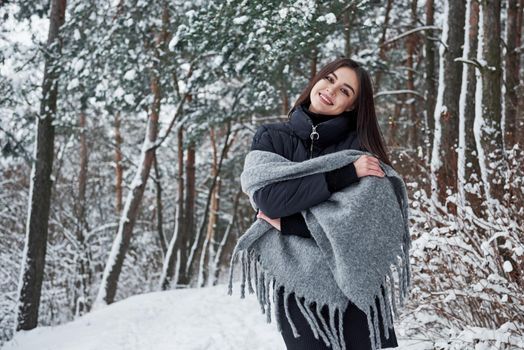 Portrait of charming woman in the black jacket and grey scarf in the winter forest.