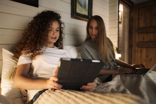 Two beautiful women lying in bed, holding and watching laptop