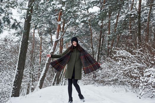 Well dressed for that season. Cheerful young girl in warm clothes have a walk in the winter forest at daytime.