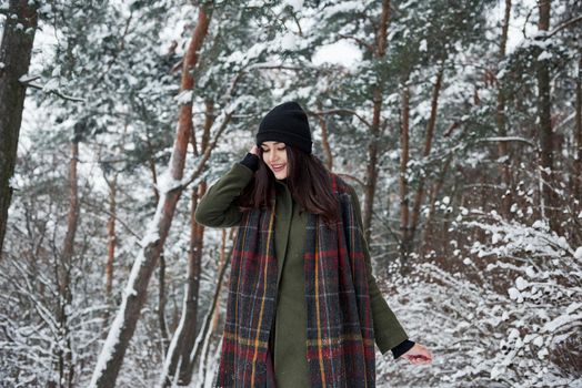 Holidays season. Cheerful young girl in warm clothes have a walk in the winter forest at daytime.