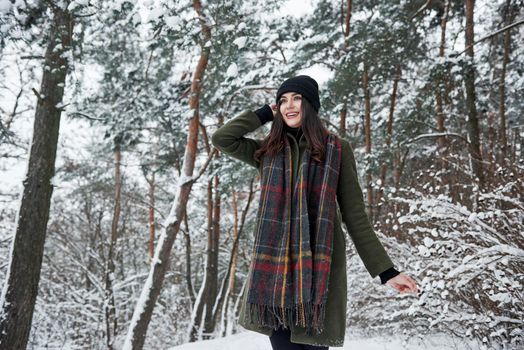 Long scarf. Cheerful young girl in warm clothes have a walk in the winter forest at daytime.