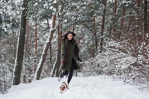 Picture in motion. Woman in warm clothes walks the dog in the snowy forest. Front view.