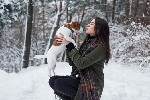 Side view. Smiling brunette having fun while walking with her dog in the winter park.