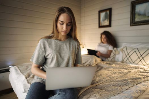 Two beautiful women lying in bed, holding and watching laptop
