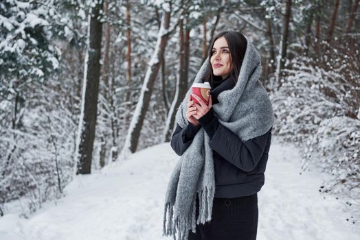 Feel the moment. Girl in warm clothes with cup of coffee have a walk in the winter forest.