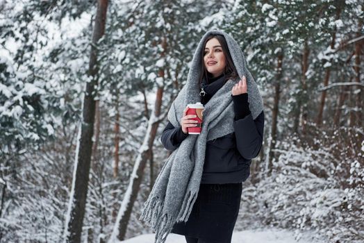 Conception of winter holiday. Girl in warm clothes with cup of coffee have a walk in the snowy forest.