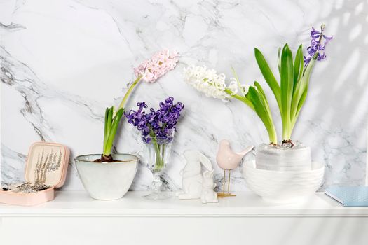 White hyacinth in a large porcelain bowl, figurines of hares and a bird, are on the fireplace against the white marble wall. Layout. Spring concept