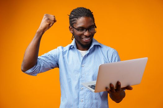 Young smiling african man standing and using laptop computer over yellow background, close up