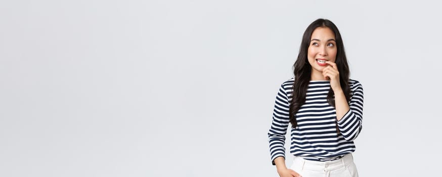Lifestyle, people emotions and casual concept. Thoughtful, dreamy and creative asian woman having plan, biting finger while pondering, thinking and looking upper left corner focused.
