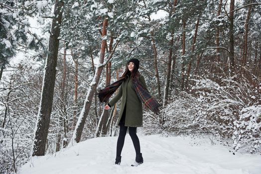 Enjoying the winter. Cheerful young girl in warm clothes have a walk in the snowy forest at daytime.