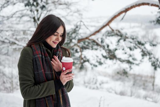 Enjoying fresh drink. Girl in warm clothes with cup of coffee have a walk in the winter forest.