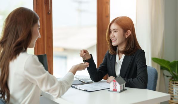 real estate agent holding house key to his client after signing contract agreement in office,concept for real estate, moving home or renting property.