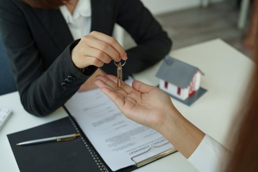 real estate agent holding house key to his client after signing contract agreement in office,concept for real estate, moving home or renting property.